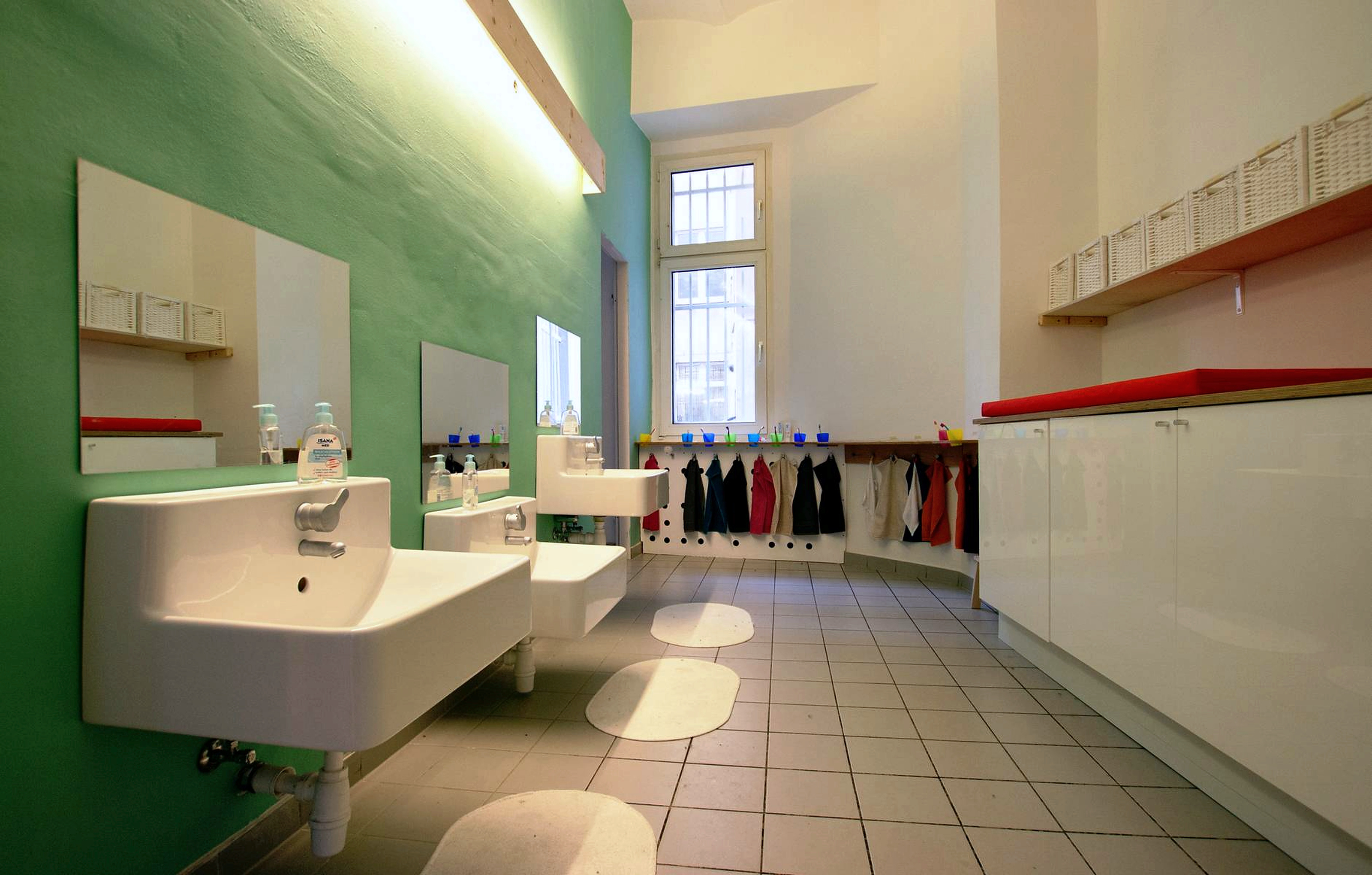 Kindgerechter Sanitärraum mit niedrigen Waschbecken und Garderobe